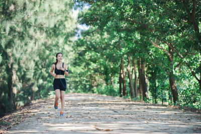 Full length of young woman jogging on road amidst trees