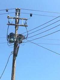 Low angle view of electricity pylon against clear blue sky