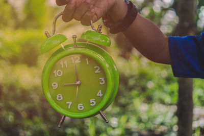 Close-up of hand holding clock against blurred background