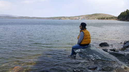 Woman sitting on rock by lake against sky