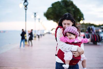 Mother carrying toddler daughter on promenade during sunset