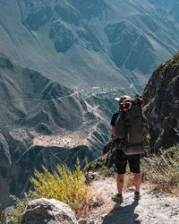 Rear view of man standing on rock by mountains