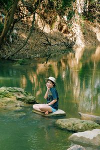 Side view of teenage boy sitting on rock by lake