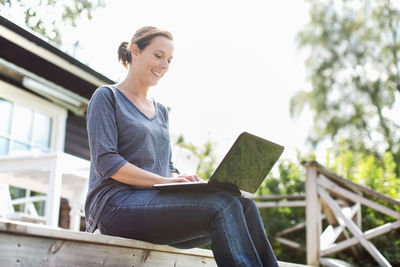 Woman using laptop on porch against clear sky