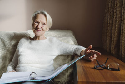 Happy senior woman with documents sitting on sofa at home