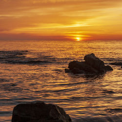 Rock formation in sea against sky during sunset