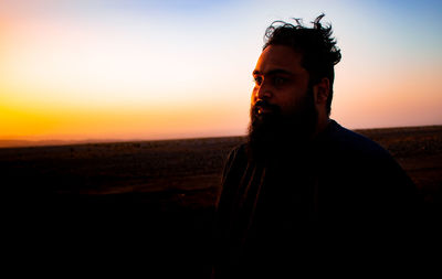 Side view of man looking away against sky during sunset