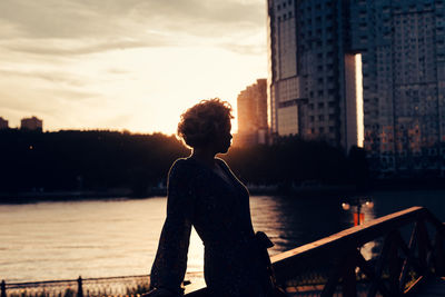 Woman standing at railing against river during sunset