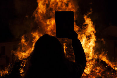 Rear view of silhouette woman standing with book against bonfire at night