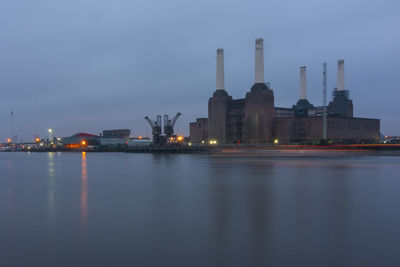Illuminated factory by lake at dusk
