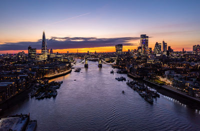 River amidst illuminated buildings against sky during sunset