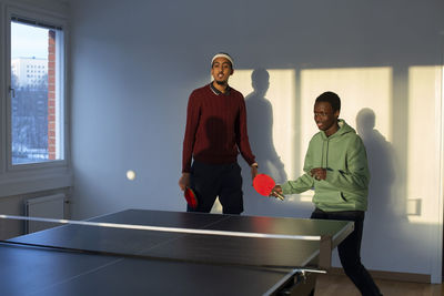 Friends playing table tennis in games room
