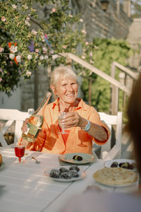 Senior woman holding alcohol bottle while sitting at dining table in back yard