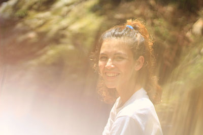 Portrait of smiling woman against trees during sunny day