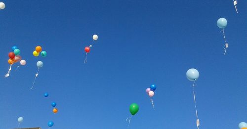 Low angle view of helium balloons flying against clear blue sky