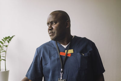 Male doctor wearing scrubs against wall at hospital