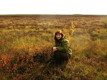 High angle portrait of young woman in warm clothing crouching on grassy field