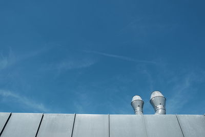 Low angle view of smoke stacks on roof against blue sky