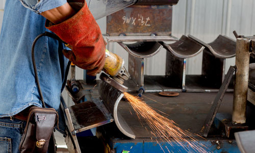 Midsection of manual worker working on metal structure in factory