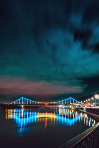 Illuminated bridge over river against sky at night