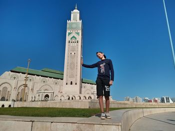 Man standing by building against clear blue sky