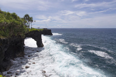 Volcanic coastal cliffs with blue waves breaking during sunny day