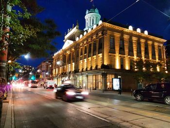 Cars on road by illuminated buildings in city at night