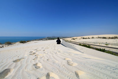 Rear view of woman sitting at beach against clear blue sky