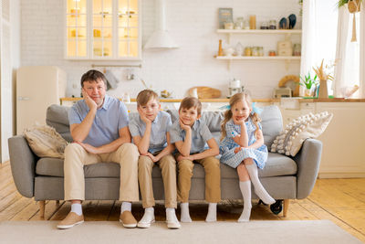 Smiling father with three small children are sitting at home on the sofa