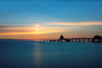 Silhouette pier over sea against dramatic sky during sunset