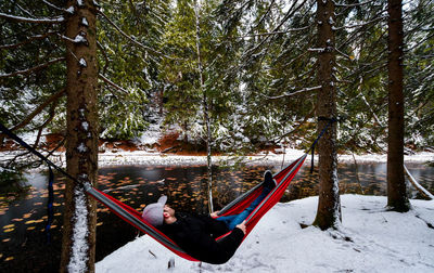 Man resting in hammock on snow covered field by lake