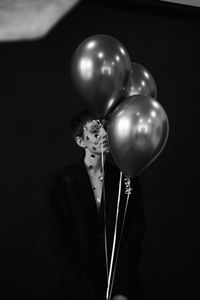 Midsection of man holding balloons against black background