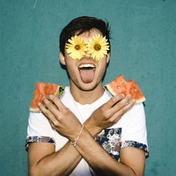 Man holding watermelon slices with eyes covered by flowers against wall