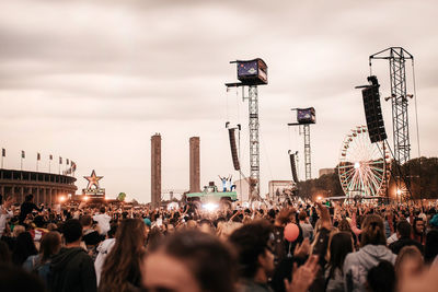 Crowd at concert against sky in city during sunset