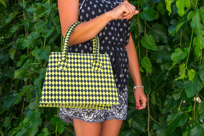 Midsection of woman holding purse against plants