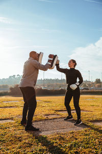 Full length of woman and man exercising on field against sky