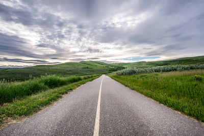 Empty road amidst field against sky