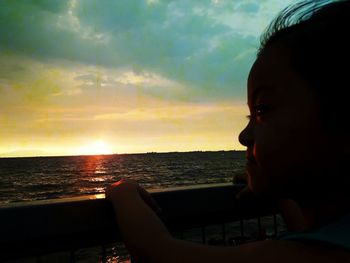 Close-up of boy looking at sea against sky during sunset