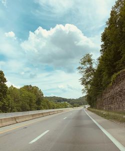 Empty road by trees against sky