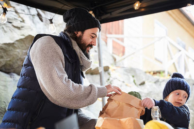 Girl buying broccoli while male vendor holding paper bag at market stall