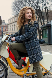 Young woman standing with bicycle on roadside in city during winter