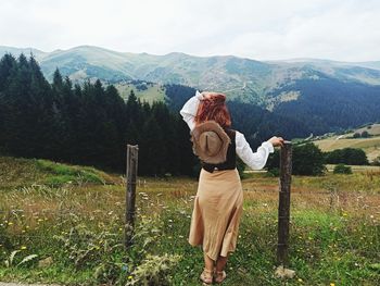 Rear view of woman standing on field against mountains