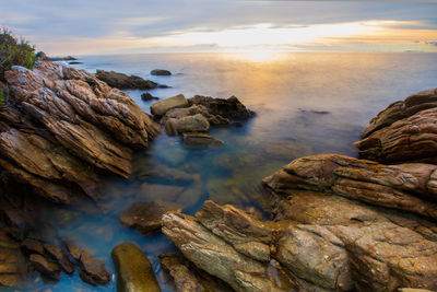 Rocks in sea against sky during sunset