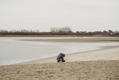 Cute boy on sandy beach kneeling down to study findings