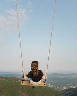 Rear view of woman sitting on swing against mountains