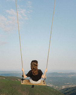 Rear view of boy sitting on swing at playground