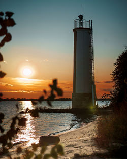 Silhouette lighthouse by sea against sky during sunset