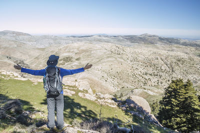 Rear view of man with arms outstretched standing on mountain