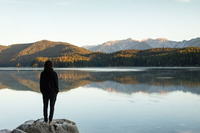 Rear view of man standing on rock by lake against sky