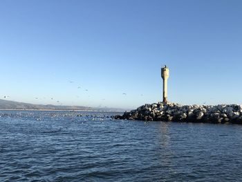 Lighthouse by sea against clear blue sky